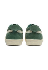 Groene suède sneakers met een structuurbeige rubberen zool, voorzien van een ronde hiel tab en contrasterende zijstrepen. Achteraanzicht.