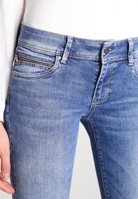 Niebieskie dżinsy o slim fit, pięciokieszeniowym wzorze oraz ukośnej kieszeni na zamek z metalowymi elementami z przodu.