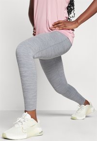 Leggings grises con una textura jaspeada, diseño ajustado, combinados con zapatillas blancas y una camiseta deportiva rosa.