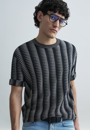 Kortærmet sweater med mønstret design i sort og grå, rund halsudskæring og opkrogede ærmekanter, kombineret med lyseblå denim.