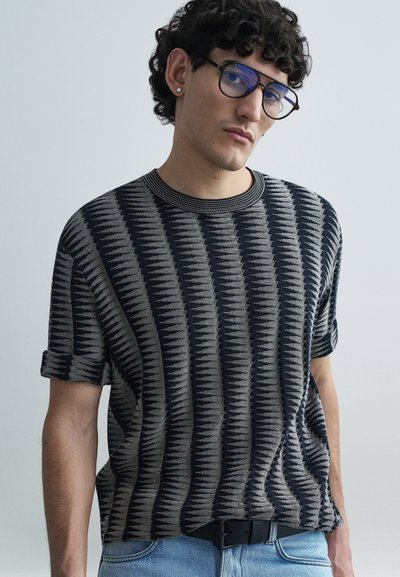 Pull à manches courtes avec un motif en noir et gris, encolure ronde et poignets retroussés, associé à un jean denim bleu clair.