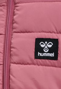 Różowa pikowana kurtka z zamkiem błyskawicznym, teksturowanym materiałem i czarną metką z białym logo, które brzmi "hummel."