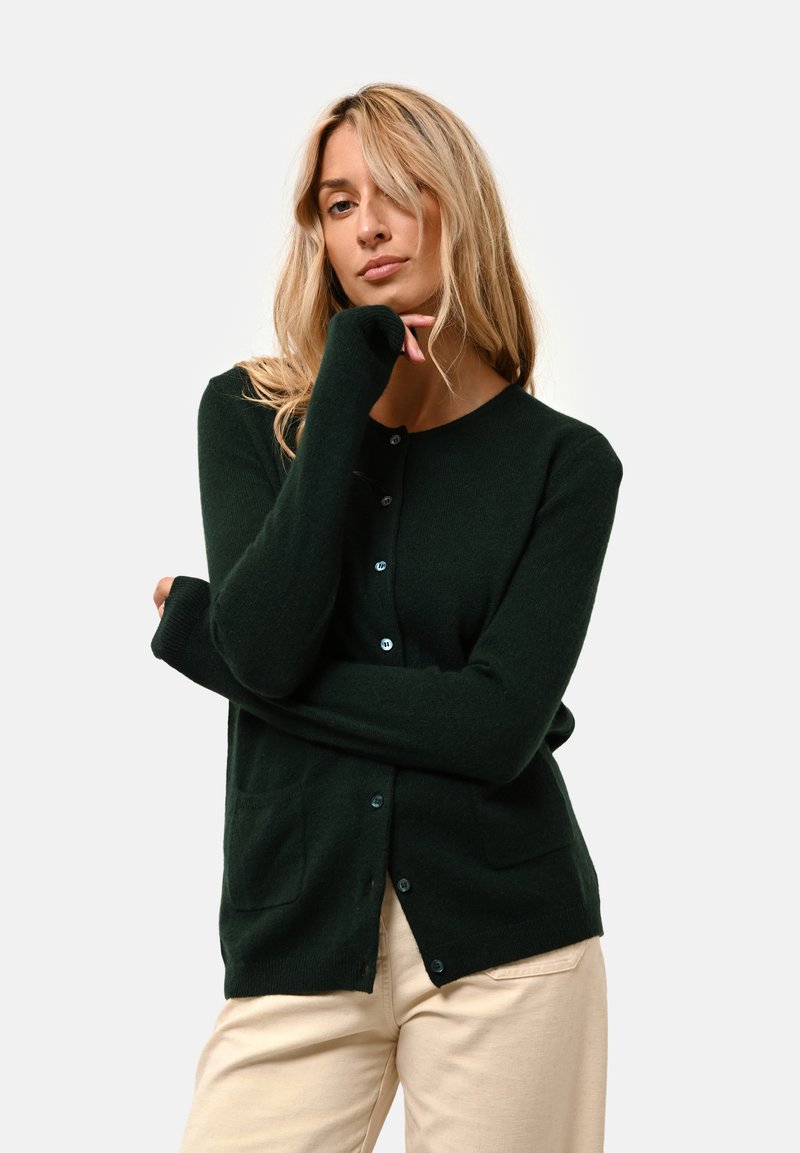 Cardigan verde scuro realizzato in tessuto morbido, con scollatura arrotondata, bottoni frontali e due tasche laterali. Maniche lunghe con polsini a coste.