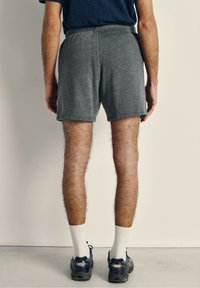 Pantalones cortos deportivos grises, hechos de tela suave, con una cinturilla elástica. Combinados con calcetines blancos y zapatillas oscuras.