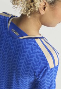 Blauw shirt met een bladerenpatroon, accentueert door een gouden kraag en drie strepen. Bevat de tekst "Azzurra" op de achterkant van de halslijn. Soepele stof textuur.