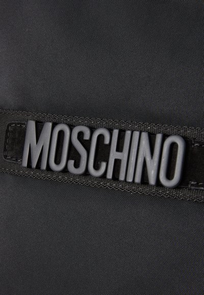 Melns neilona maisiņš ar plakanu siksnu, uz kuras ir izcelts matēts melns "MOSCHINO" logo. Gluda tekstūra ar smalku auduma austu rakstu.