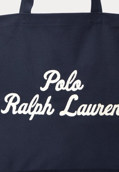 Granatowa torba na ramię z białym haftowanym napisem "Polo Ralph Lauren" oraz przeszywanymi rączkami u góry.