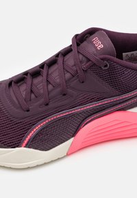 Lila Sportschuh mit einem strukturierten Mesh-Obermaterial, rosa Akzenten und einer geriffelten Gummisohle; verfügt über Schnürsenkel und ein Branding auf der Zunge.