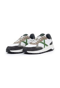 Zapatillas que combinan cuero blanco y ante gris, con costuras de acento verde, cordones blancos planos y una suela de goma negra gruesa.