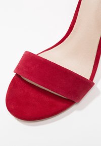 Sandale à talon haut en suède rouge avec une large bride sur le dessus, doublée d'un intérieur lisse et dotée d'un design à bout rond.