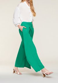 Gröna vida byxor med knytmidja i kombination med en vit, knappad skjorta. Vita sandaler med remmar och klack fulländar looken.