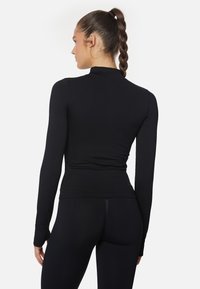 Schwarzes Langarmoberteil mit einem hohen Kragen, tailliertem Schnitt und glatter Textur, kombiniert mit passenden schwarzen Leggings.