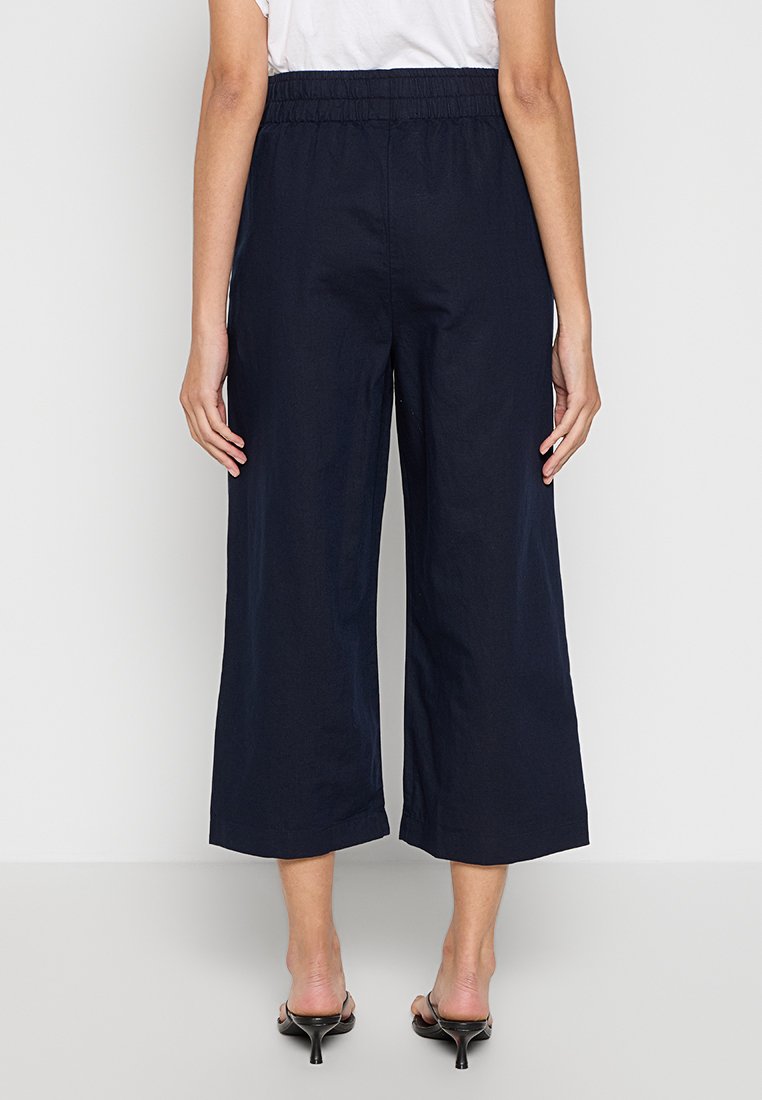 Marinefarbene, weiter Hosenbeine mit einem elastischen Bund, die eine glatte Textur und eine lockere Passform aufweisen, die bis zur Mitte der Wade fällt.
