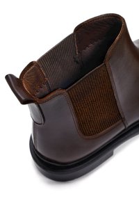 Stivale Chelsea in pelle marrone con pannello elastico laterale, linguetta sul retro e suola nera, mostrato da un angolo alto posteriore.