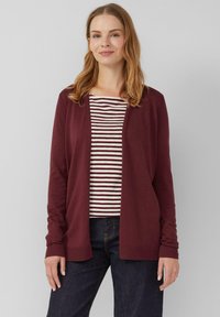 Burgunderfarbener Cardigan mit offener Front, langen Ärmeln und gerippten Bündchen, getragen über einem gestreiften burgunder- und weißen Oberteil. Dunkle Jeans runden das Outfit ab.