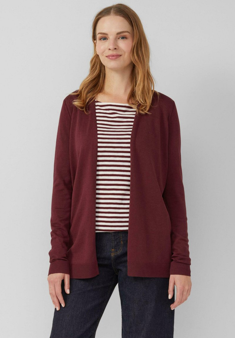 Burgunderfarbener Cardigan mit offener Front, langen Ärmeln und gerippten Bündchen, getragen über einem gestreiften burgunder- und weißen Oberteil. Dunkle Jeans runden das Outfit ab.
