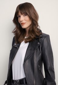 Czarna skórzana kurtka motocyklowa z srebrnymi suwakami i elementami metalowymi, noszona na białej koszuli. Modelka ma średniej długości, falowane brązowe włosy.