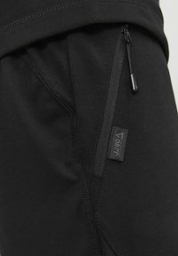Black athletic pants featuring a zippered pocket, smooth texture, and a small branded tag, designed for comfort and functionality.