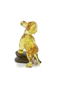 Kristallfigur föreställande ett lejon i gult med facetterad struktur, placerad på en mörk, vågig bas. Har detaljerade ansikts- och kroppskonturer.