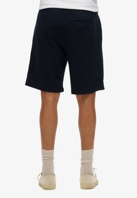 Pantaloni corti blu navy con una vestibilità rilassata, dotati di una tasca posteriore, in un tessuto misto cotone e di lunghezza sopra al ginocchio. Texture morbida e design semplice.
