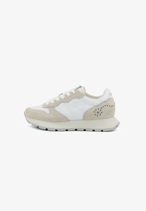 Witte en beige suède sneaker met vetersluiting, een beige zool en decoratieve perforaties nabij de hiel op een witte achtergrond.