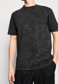 Svart t-shirt med kort ärm och en strukturerad, marmorering finish. Har en rundad halsringning och diskret logotyp på bröstet. Lätt oversized passform.