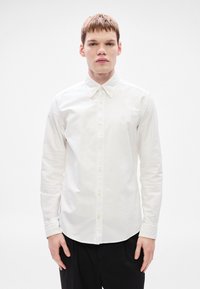 Λευκό πουκάμισο με μακριά μανίκια και κουμπιά, κατασκευασμένο από απαλό βαμβάκι, με κλασικό γιακά και κούμπωμα κουμπιών, σε εφαρμοστή γραμμή και χωρίς ορατά σχέδια.