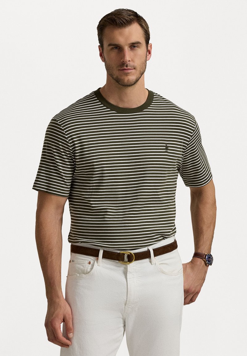 Striped crew neck T-shirt in olive green and white, short sleeves, cotton material, worn with white jeans and a brown belt.