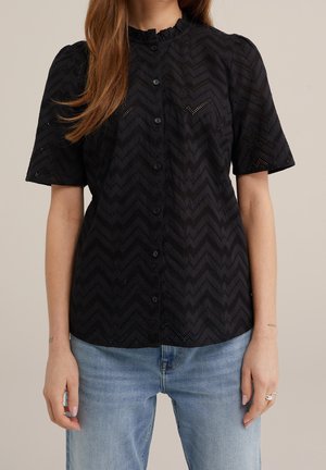 Czarna koszula na guziki z krótkim rękawem, zdobiona wzorem w jodełkę z ażurowych oczek, noszona z jasnoniebieskimi dżinsami, ukazująca talię i ramiona.