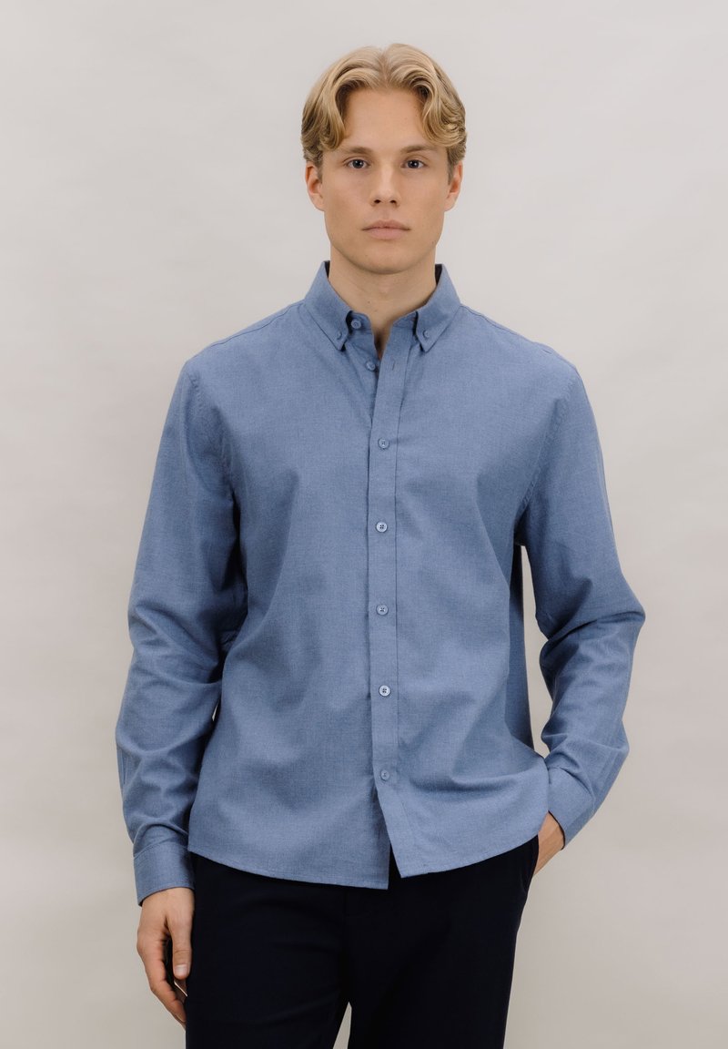 Lys blå skjorte med knapper laget av vevd stoff, med klassisk krage, lange ermer og rett kant med fem knapper foran.
