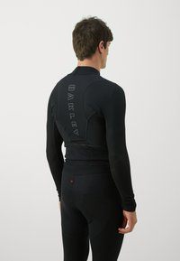 Black athletic top with a high collar and mesh back detail. Features "OAKLEY" branding in a vertical layout along the back. Fitted design.