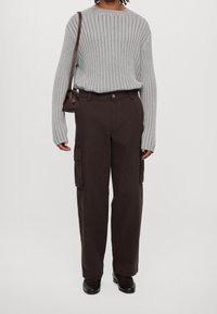 Harmaa ribbineulospaita yhdistetty tummanruskeisiin cargo-housuihin, joissa on sivutaskut, rento istuvuus ja mustat kengät. Myös ruskea käsilaukku näkyvissä.