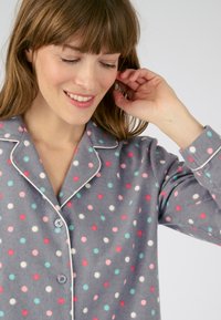 Maglione di pigiama grigio in felpa con pois multicolori in rosa, blu e bianco. Presenta un colletto a punta e una chiusura con bottoni, con dettagli in piping.