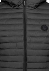 Schwarze Daunenjacke mit horizontalen Nähten, einem Reißverschluss vorne und einem tonalen Logo-Patch auf der linken Seite. Weiche Textur, entworfen für Wärme.