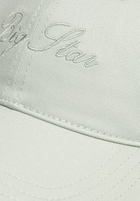 Gaiši zaļš beisbola cepures izgatavota no auduma ar izšuvumu "Big Star" logotipu. Iezīmēta ar struktūru un noapaļotu vizieri ar redzamām šuvēm.