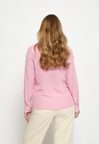 Langærmet bluse i lyserød, lavet af glat stof med en subtil glans og knaplukning ved manchetterne, kombineret med vide beige bukser.