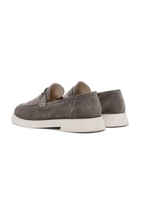 Zapatos gris de ante tipo slip-on con suela de goma blanca, que presentan costuras mínimas y un diseño de punta redondeada. Los detalles incluyen un sutil acento lateral.