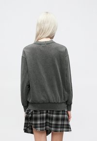 Felpa grigia con vestibilità rilassata, orlo a coste e maniche lunghe, abbinata a una gonna a quadri bianca e nera con bordo sfrangiato.