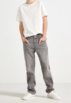 Šedé džíny z denimu s rovnými nohavicemi, předními kapsami a jemným vyblednutím, doplněné jednoduchým bílým tričkem s krátkým rukávem a bílými teniskami.