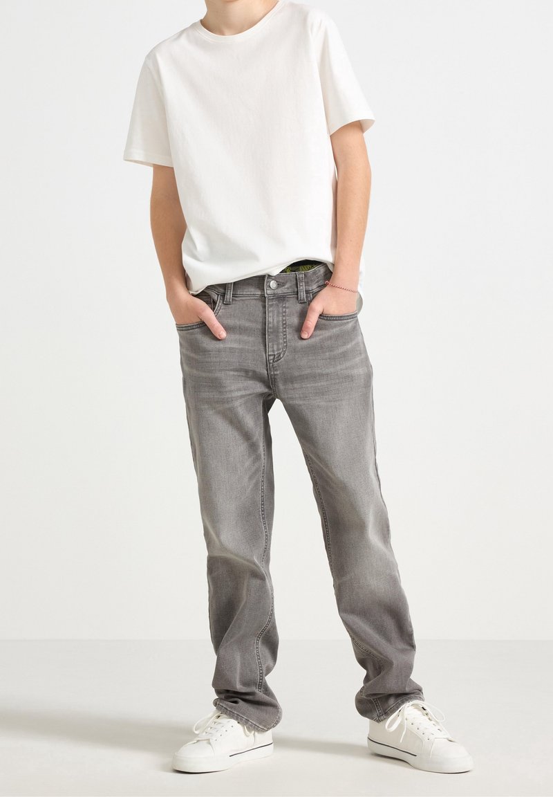 Jean en denim gris à coupe droite, poches avant et légère décoloration, associé à un t-shirt blanc uni à manches courtes et des baskets blanches.