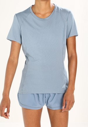 Personne portant un t-shirt de sport bleu clair à manches courtes et un short assorti, debout avec les bras détendus le long du corps sur un fond uni.