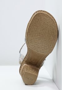 Korkosandaali, jossa on teksturoitu ruskea kumiulkopohja ja oljenkaltaiset korkokengät. Yläosa esittelee värikkäitä kangashihnoja vaaleansinisellä sävyllä.