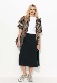 Veste bomber à imprimé léopard, t-shirt blanc, jupe midi noire et baskets argentées, avec un sac à épaule gris, sur un fond uni.