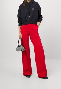 Svart huvtröja med en logotyp, tillsammans med högmidjade, vida röda byxor. Accessoarer inkluderar en liten, metallisk handväska. Svarta skor.