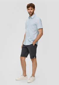 Lichtblauw T-shirt met korte mouwen en een geometrisch patroon, gecombineerd met grijze opgerolde shorts en witte sneakers. Eenvoudig ontwerp en kleuren.