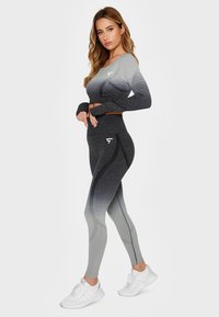 Grå ombre træningssæt bestående af en tætsiddende langærmet cropped top og højtaljede leggings med buede sømme og logo detaljer.