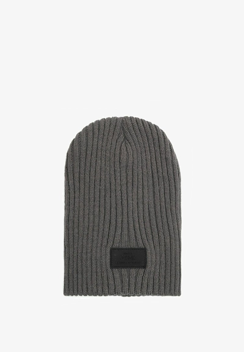 Szara dzianinowa czapka z dużym splotem, miękki materiał oraz prostokątna czarna łatka z wypukłym napisem z przodu.