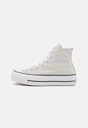 Zapatillas altas de lona blanca con suela de goma, detalle de franja negra y ojales blancos, con punta redondeada y textura suave.