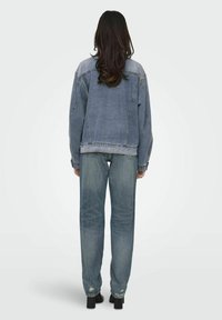Giacca di jeans con vestibilità rilassata, colore azzurro chiaro e texture sbiadita, abbinata a jeans a gamba dritta in una tonalità simile e scarpe con tacco quadrato.
