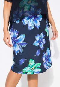 Námorní sukně s velkými modrými a zelenými hibiskovými vzory, vyrobená z měkké, pružné tkaniny s přiléhavým střihem a zakřiveným spodním lemem.